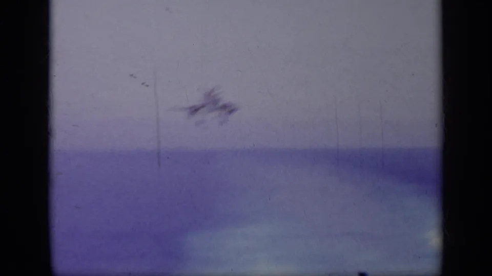 1963 Greece 8mm frame with a blurred jet above open water, seen through dark film gate bars and a purple-blue color cast.