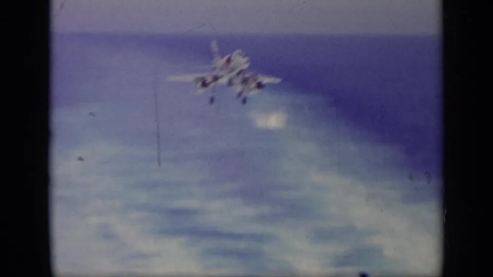 1963 Greece 8mm frame showing a blurred military jet over water and cloud haze, with dust, scratches, and soft exposure.