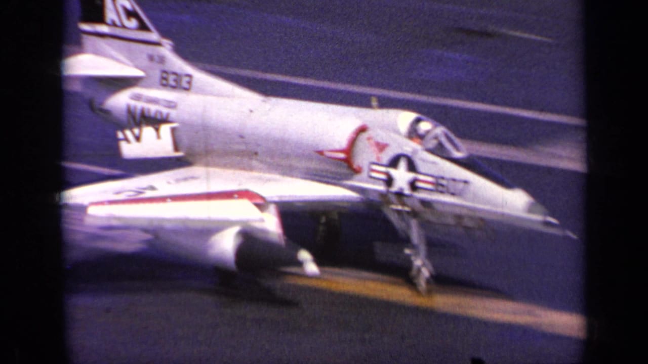 1963 Greece home-movie frame of a U.S. Navy jet landing on an aircraft carrier, with tail code and deck markings visible.
