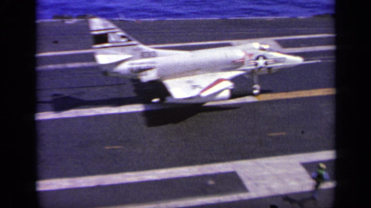 Navy jet rolls along the carrier deck with the blue ocean behind it.