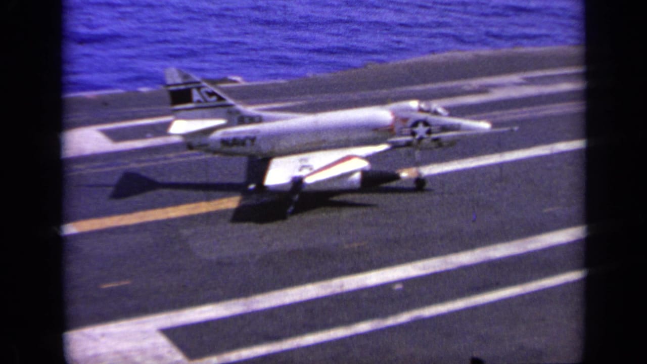 Navy-marked jet continues along the carrier deck near the ocean.