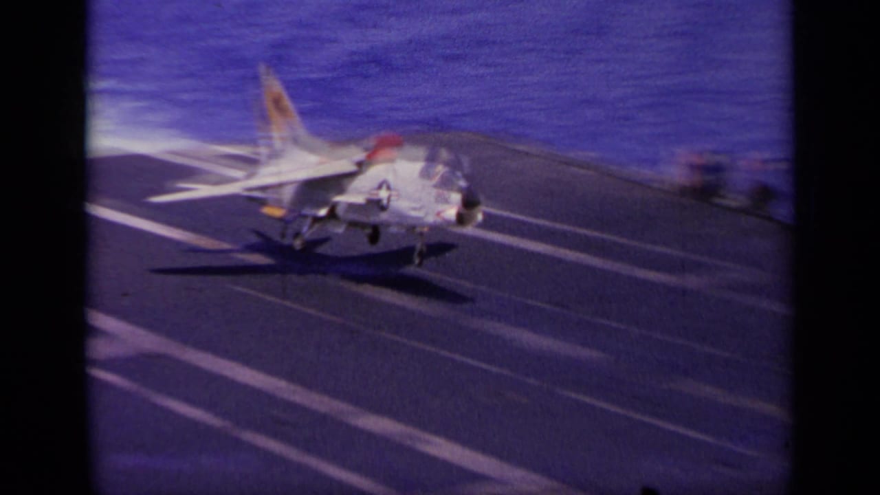 Navy jet touches down on an aircraft carrier deck with ocean beyond.