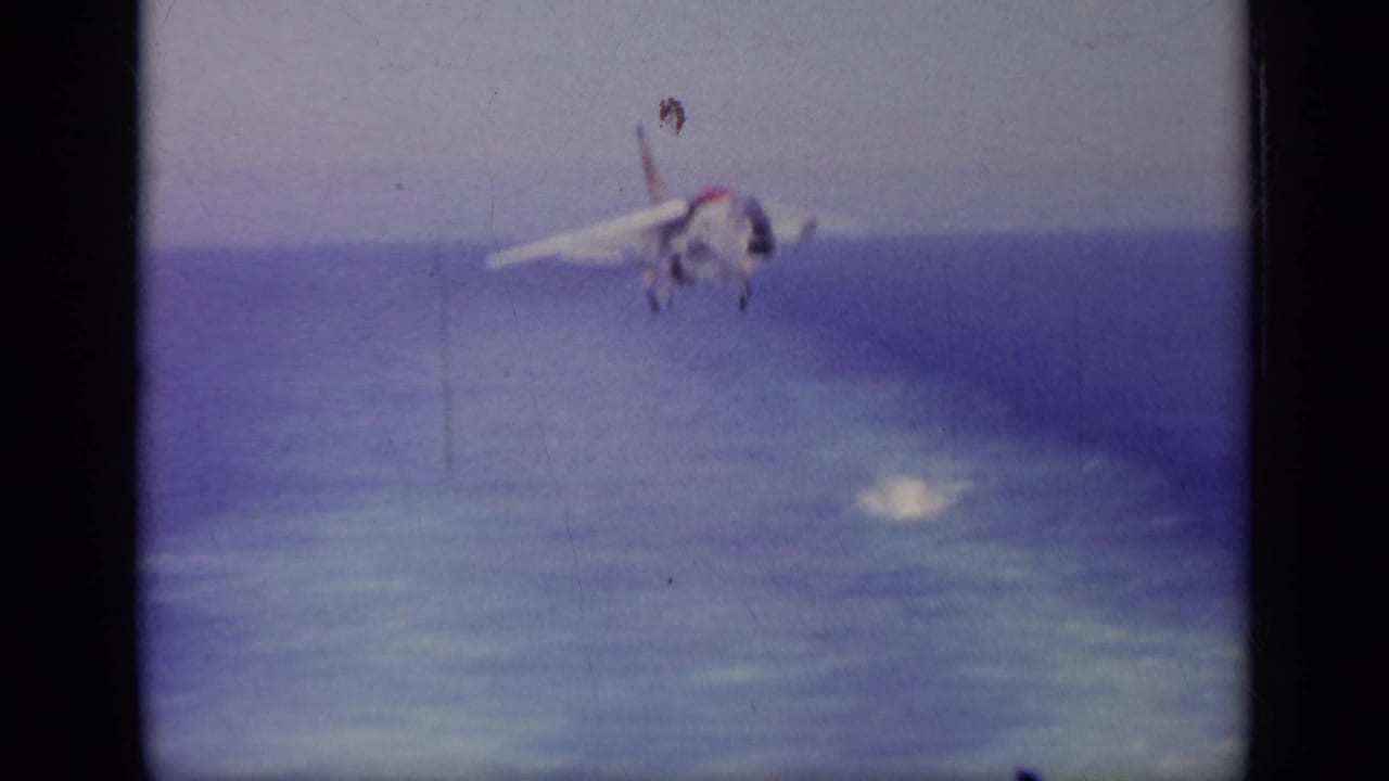 1963 8mm frame of a U.S. Navy jet appearing to approach over the sea, seen through soft, faded home-movie film.