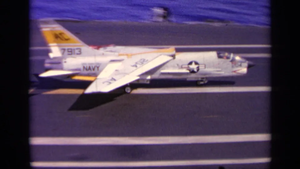 1963 8mm frame of a U.S. Navy jet taxiing on a carrier deck, with tail number 7913 and national insignia visible.