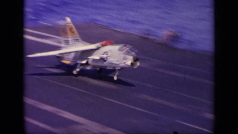 The marked Navy jet is low on the carrier deck with landing gear down, captured in a blurred 8mm frame.