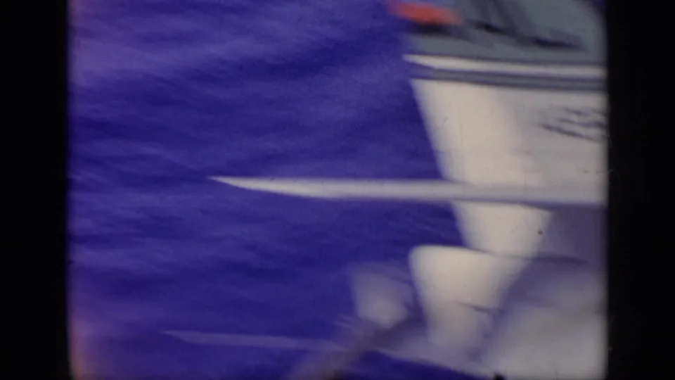 Close, partial 8mm view of a military aircraft surface at frame edge, with blue ocean and motion blur behind it.