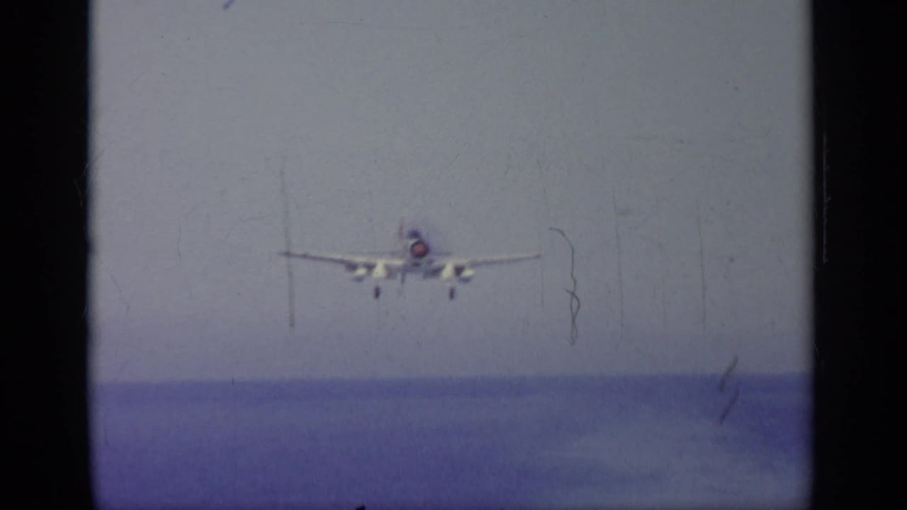 Naval jet approaching head-on above the sea, landing gear visible.
