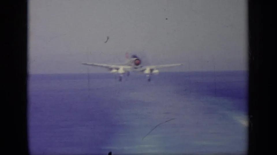 Naval jet descends toward a carrier landing approach over the sea, framed by faded 8mm color and gate shadows.