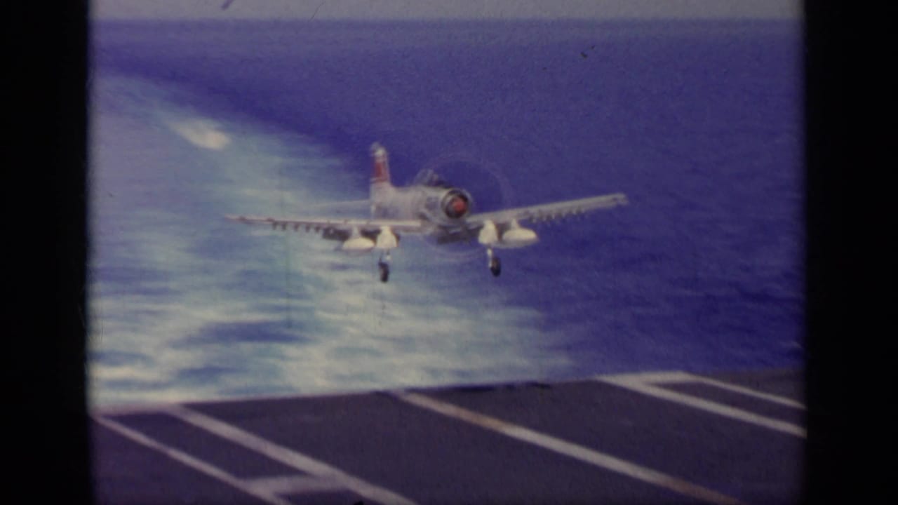 1963 8mm footage near Greece shows a white U.S. Navy-style propeller aircraft approaching a carrier deck with ocean behind it.
