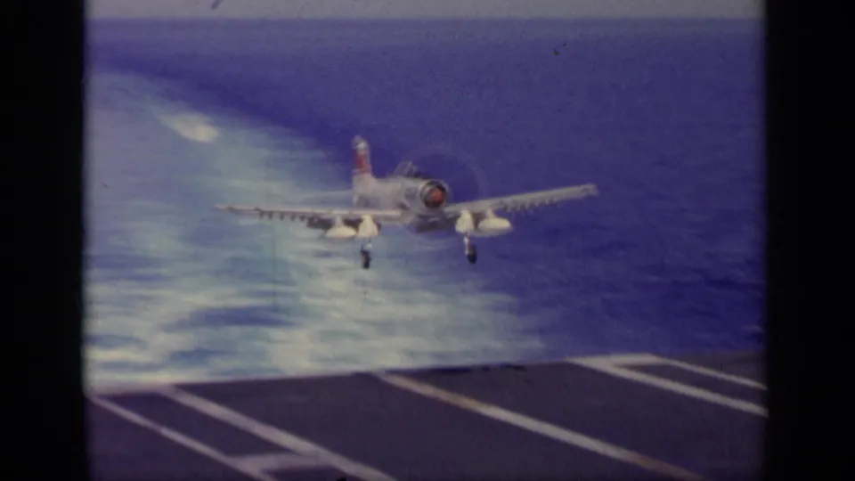 1963 8mm footage near Greece shows a white U.S. Navy-style propeller aircraft approaching a carrier deck with ocean behind it.