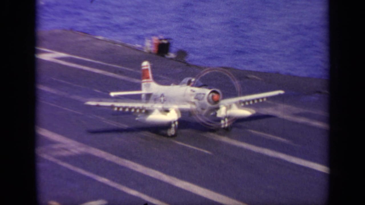 White military aircraft lands on a carrier deck with ocean in the background.
