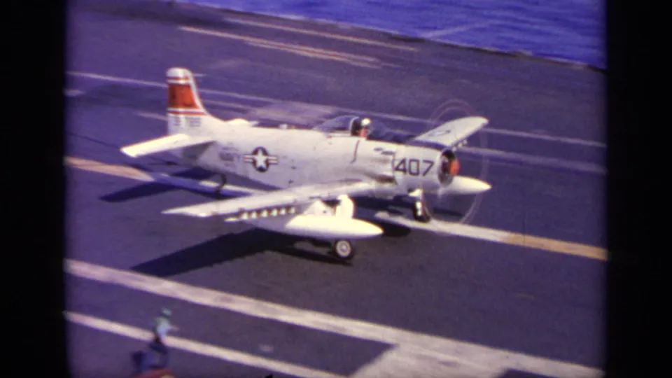 The aircraft numbered 407 rolls along the carrier deck, with runway stripes, U.S. insignia, and a small deck crew figure visible.
