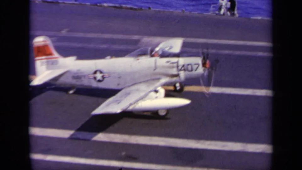 1963 Greece reel frame showing a white U.S. Navy propeller aircraft marked 407 moving on a carrier deck with ocean beyond.