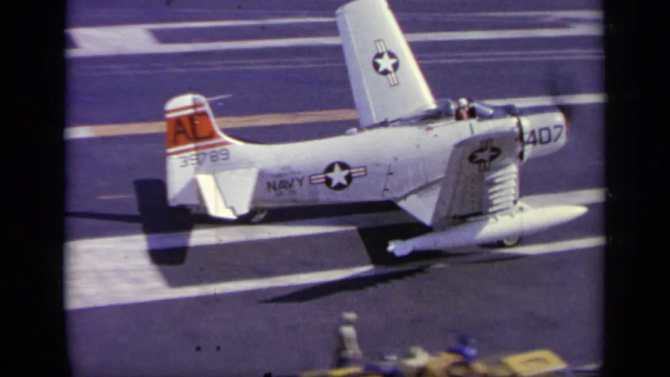 Rear-side view of the U.S. Navy aircraft with folded wings, tail code AL, and carrier deck striping in the 1963 Greece footage.