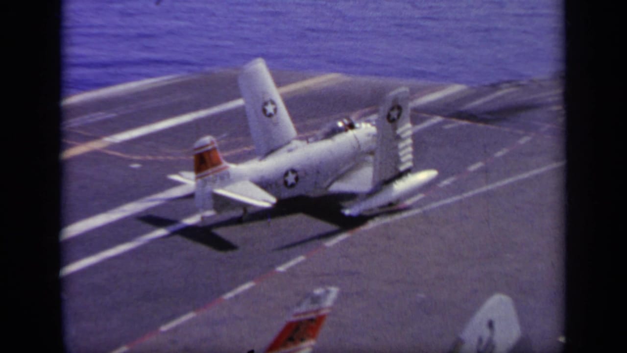 White U.S. Navy aircraft on a carrier flight deck with ocean beyond.