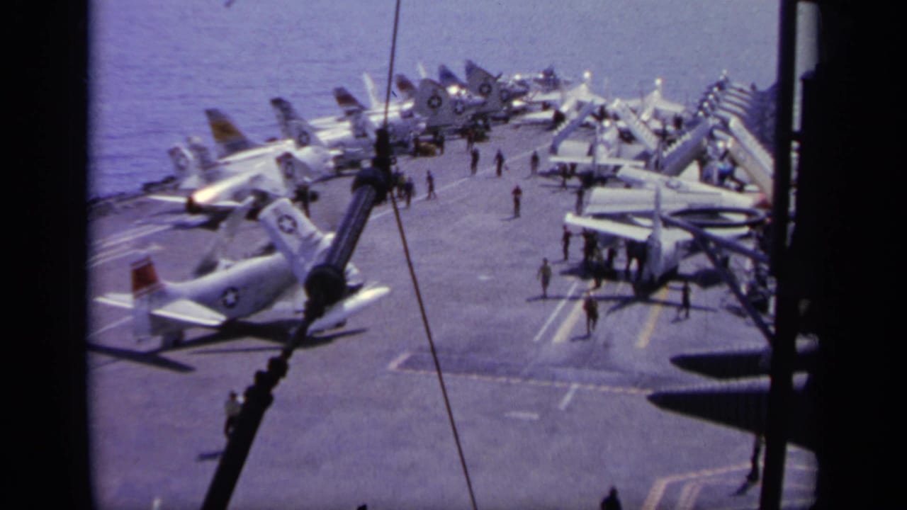 High view of parked military jets on an aircraft carrier deck at sea.