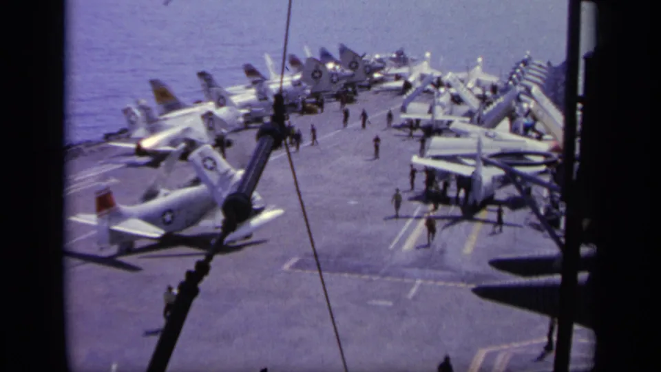1963 Greece 8mm footage showing parked military jets and small crew figures on an aircraft carrier flight deck at sea.