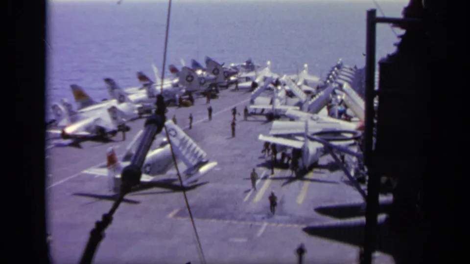 High-angle 1963 Greece carrier-deck view with several military jets parked near the ocean horizon and crew figures nearby.