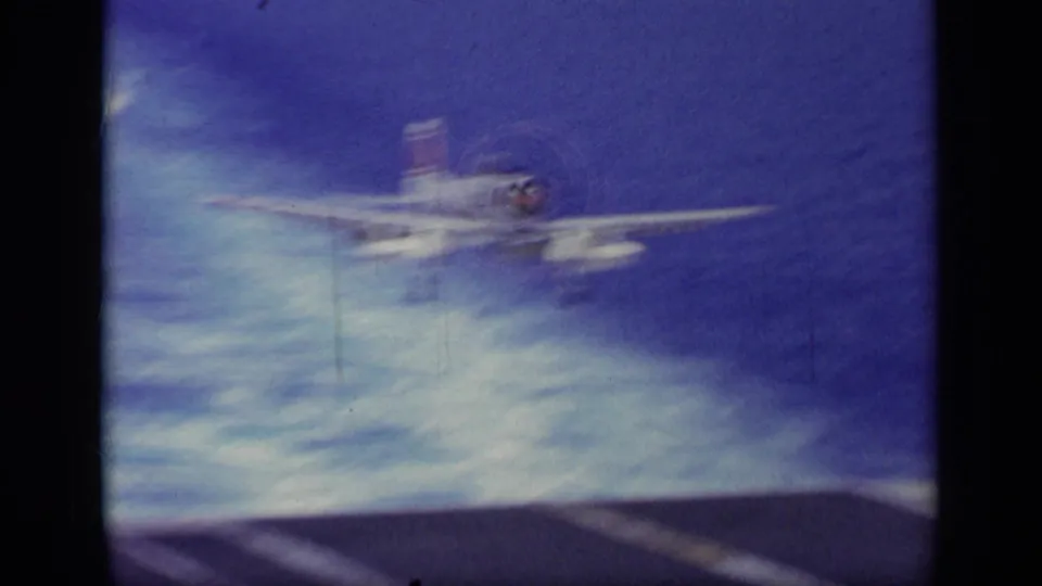 Soft 8mm frame of a military jet approaching above the ocean, likely during a carrier landing sequence in 1963 Greece footage.