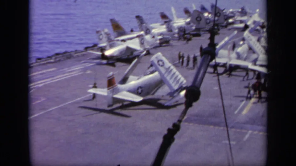 1963 Greece 8mm view of a carrier flight deck with parked military jets, deck crew, and the sea visible beyond the ship.