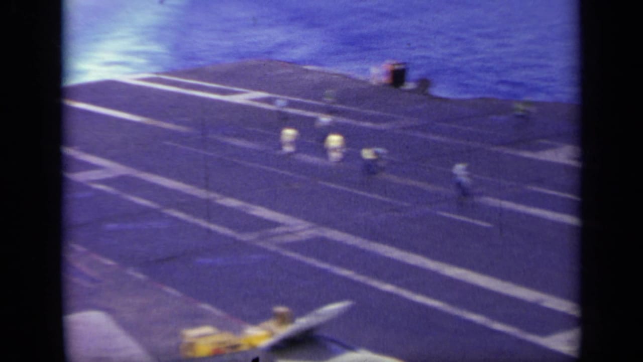 Carrier flight deck edge with open sea beyond and small deck figures.