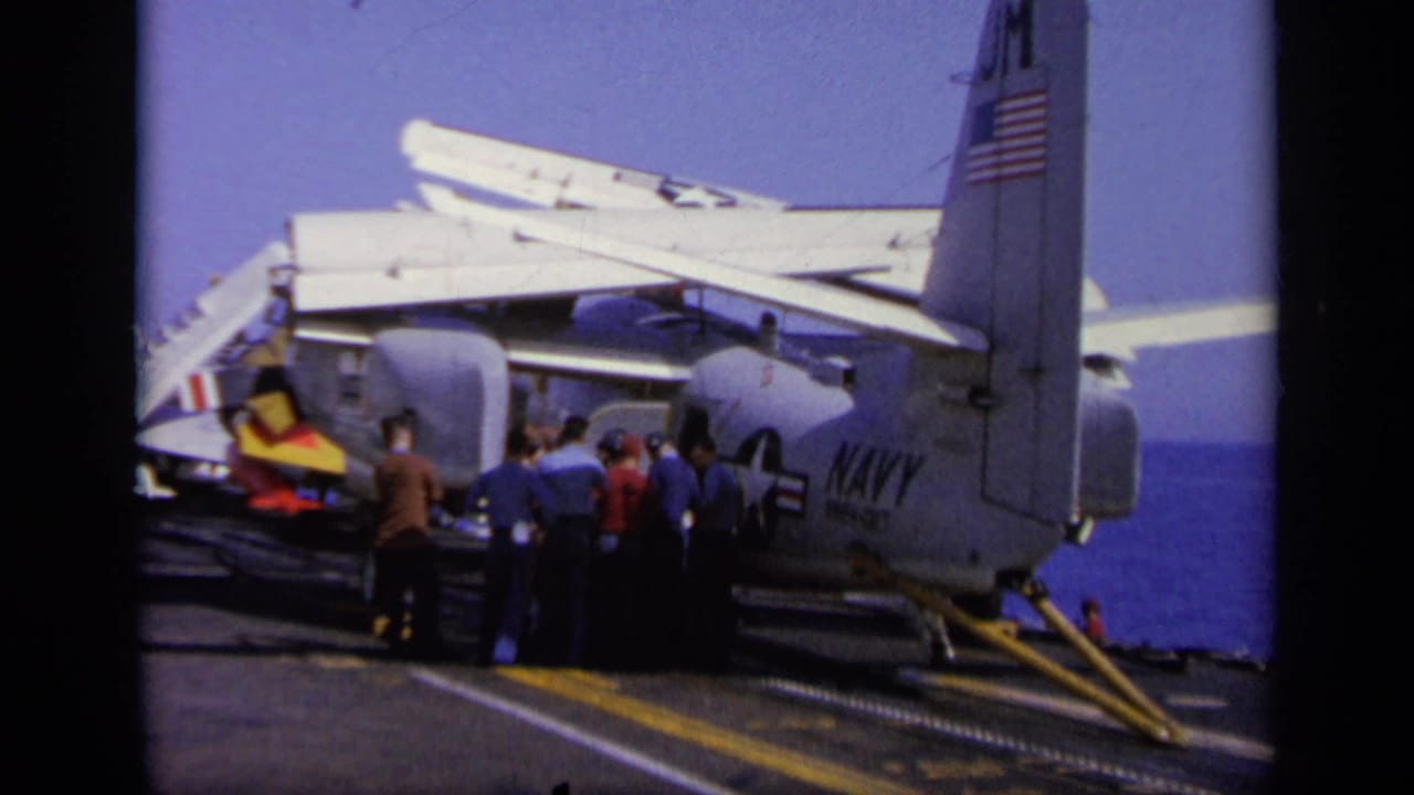 Flight deck crew near a U.S. Navy aircraft tail on an aircraft carrier at sea.