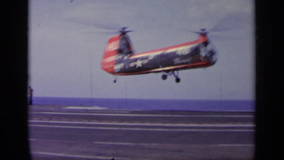 The U.S. Navy-marked tandem-rotor helicopter hovers low above the carrier deck in this 1963 Greece home-movie frame.