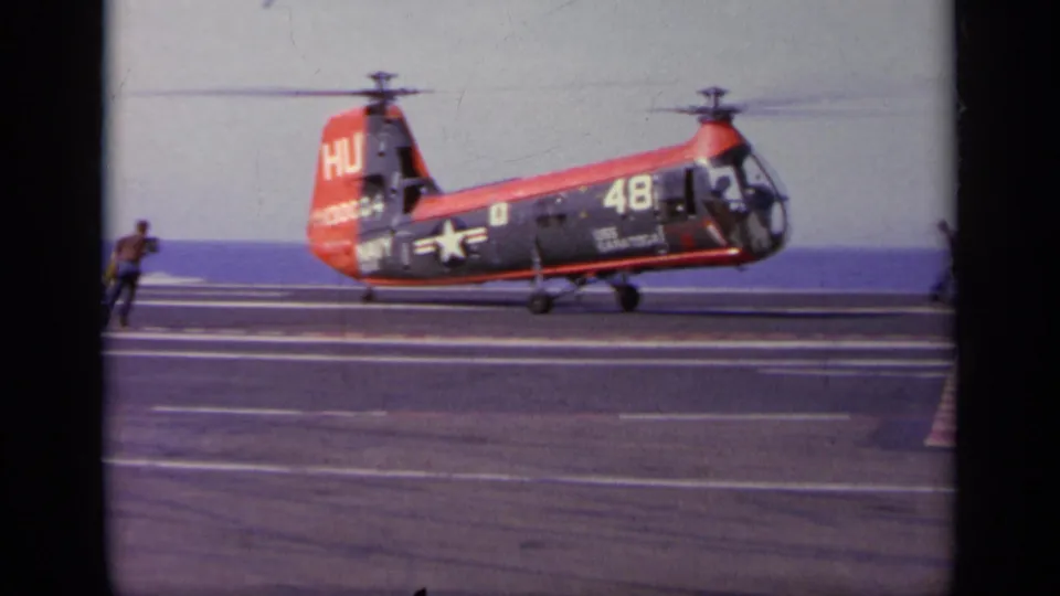 1963 Greece footage showing the U.S. Navy aircraft at deck level on the carrier, with crew figures near the edge of the frame.