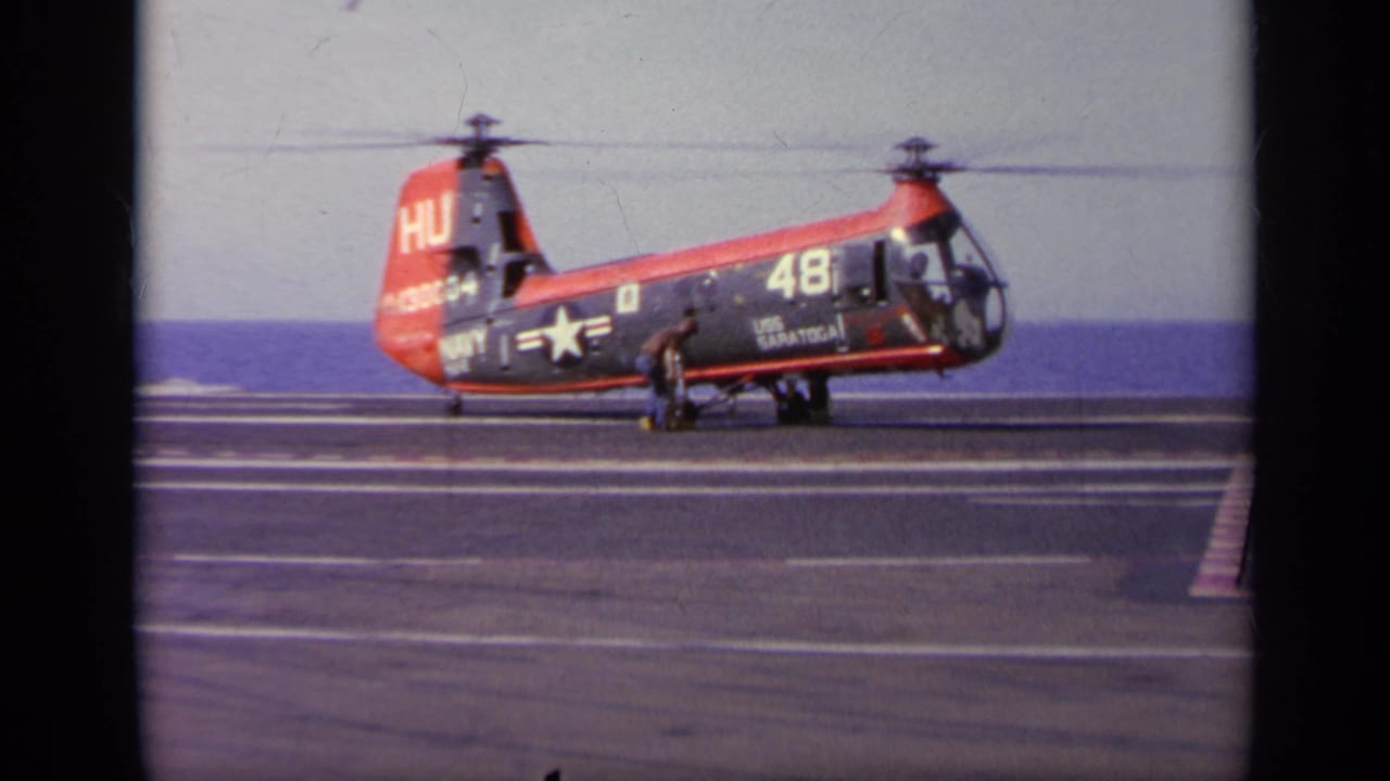 Navy rotorcraft marked 48 on a carrier deck with a crew member standing near the side.