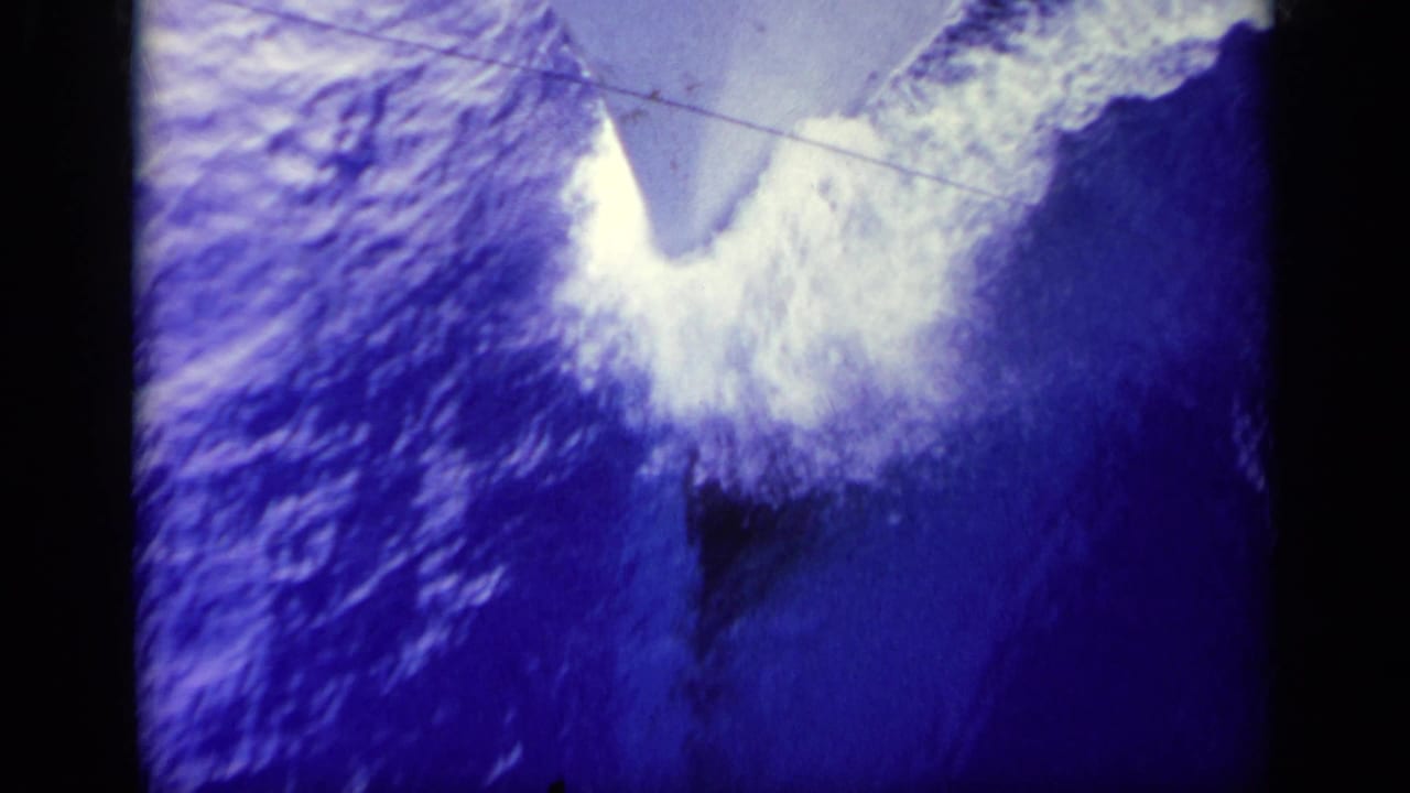 1963 Greece 8mm frame showing a gray ship bow pushing through deep blue water and frothy white wake.
