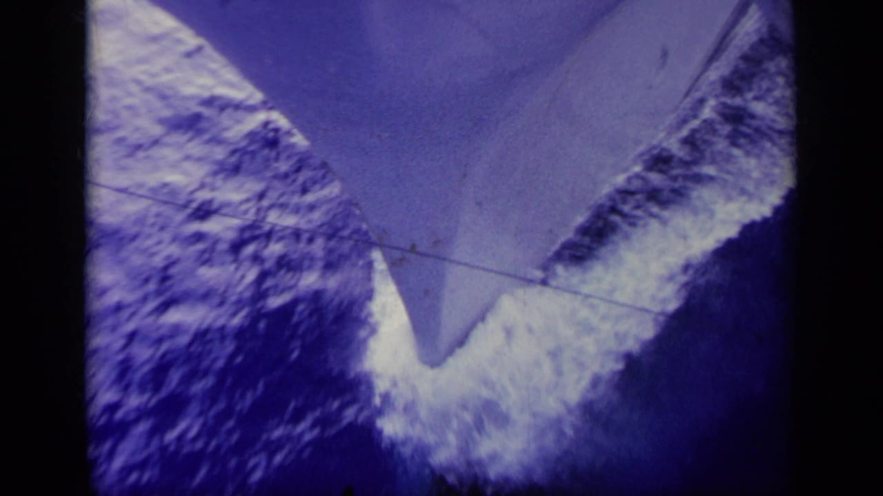 Ship bow angled over churning blue water and white wake.