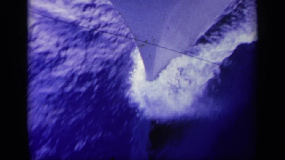Tight 8mm view of a boat bow breaking waves in Greece, with blue tint, heavy spray, and visible film wear.