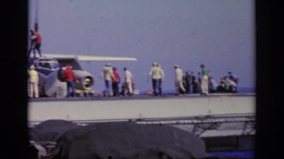 1963 Greece 8mm frame showing deck crew around a propeller plane on an aircraft carrier, with ocean and sky behind them.