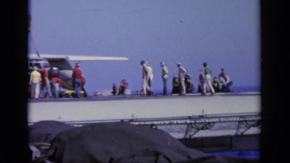 1963 Greece shipboard scene with workers standing near a military aircraft, seen from a distant 8mm home-movie viewpoint.