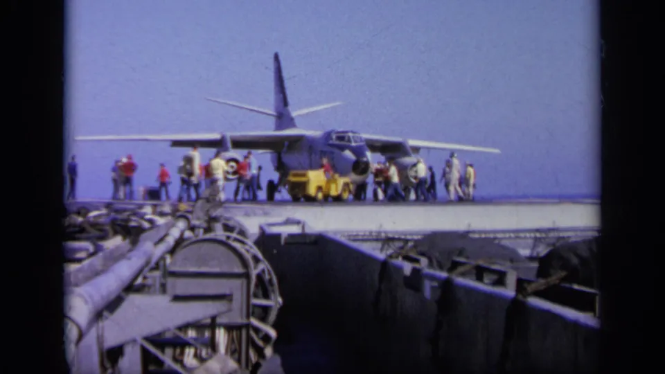 1963 Greece 8mm frame showing a military aircraft on a carrier deck, with personnel around the nose and sea in the background.
