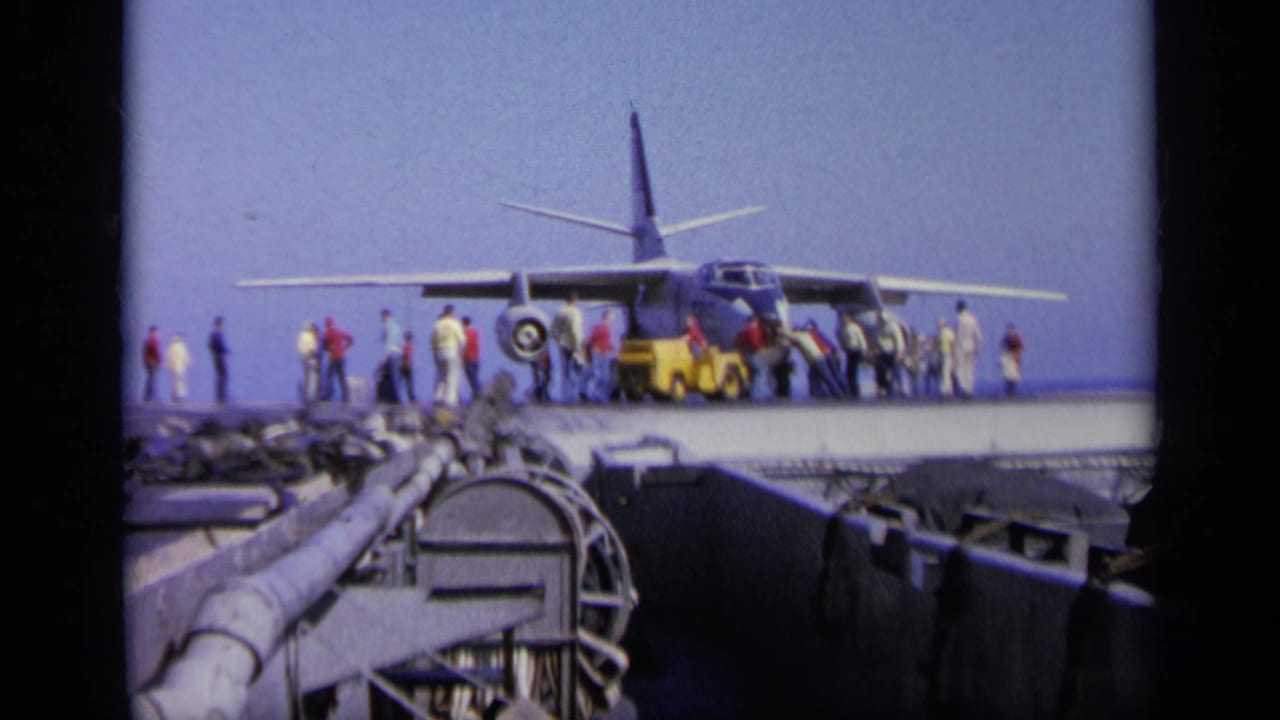 Aircraft on carrier deck with crew and onlookers spread along the wing line.