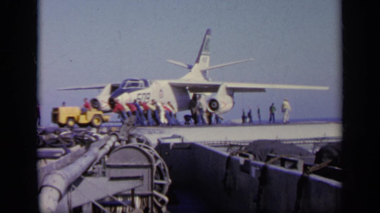 1963 Greece 8mm frame of crew clustered near a Navy jet on an aircraft carrier, with deck equipment in the foreground.