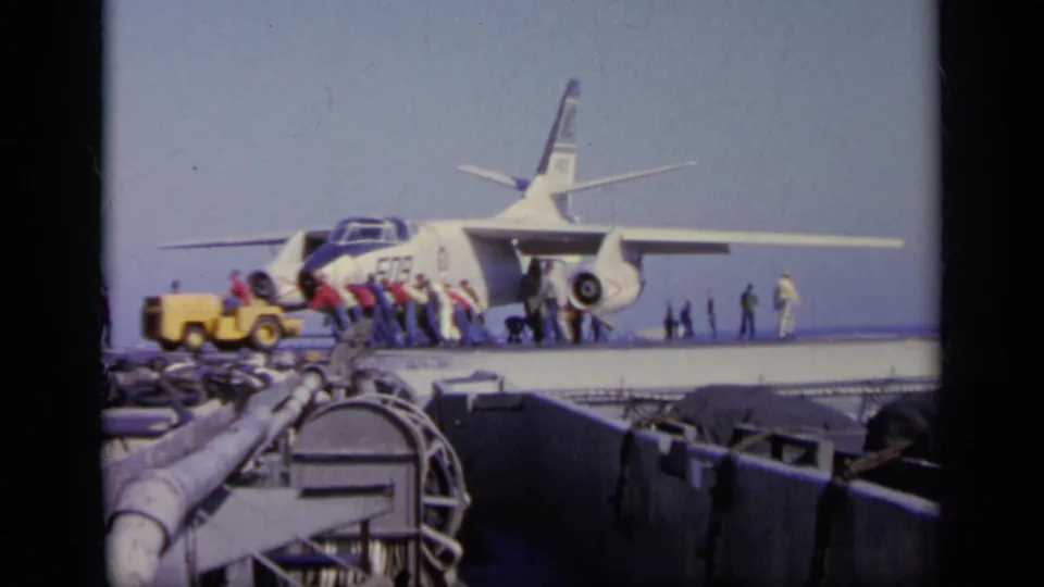 1963 Greece 8mm frame of crew clustered near a Navy jet on an aircraft carrier, with deck equipment in the foreground.
