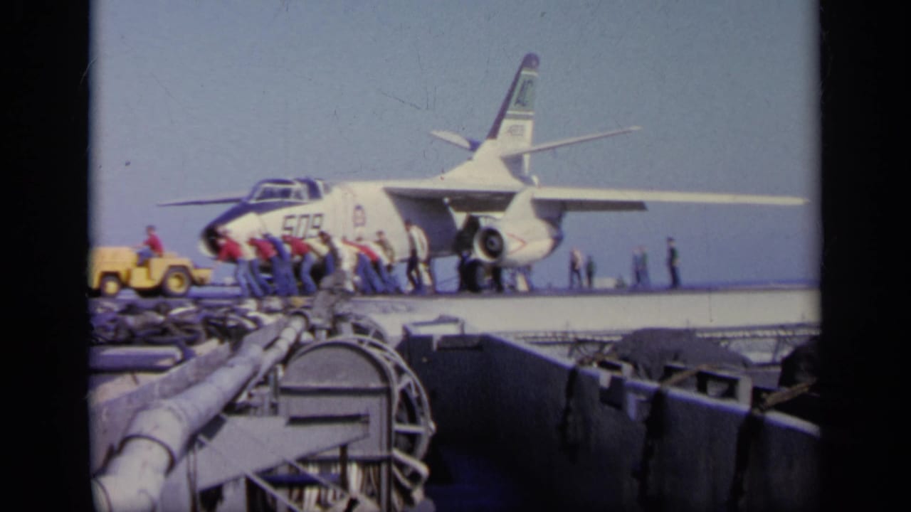 1963 Greece 8mm frame of carrier deck activity around a U.S. Navy jet, viewed from behind deck structures.