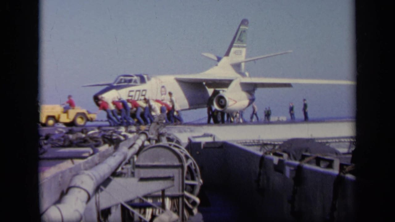 1963 Greece 8mm frame showing a military jet marked 509 on a carrier deck as crew and a yellow tow vehicle work near the nose.