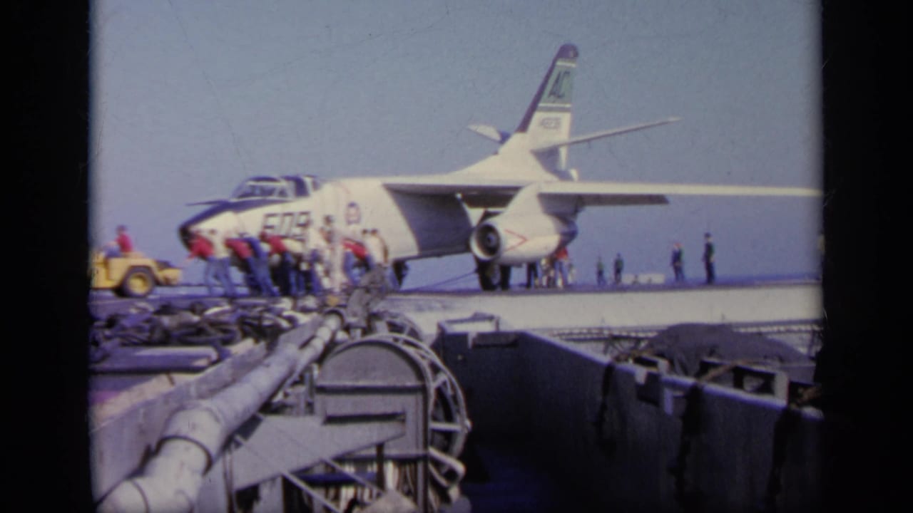 1963 Greece 8mm frame with deck crew gathered around the nose of jet 509 while carrier equipment fills the foreground.