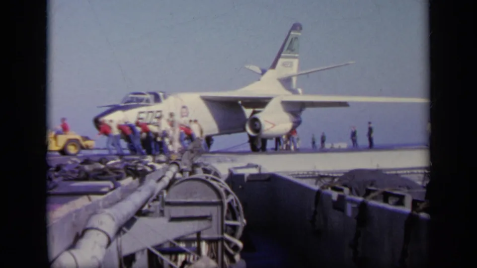 1963 Greece 8mm frame with deck crew gathered around the nose of jet 509 while carrier equipment fills the foreground.