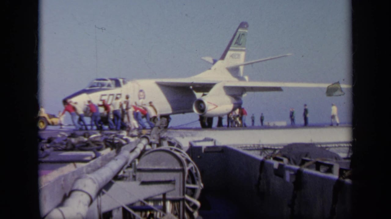 1963 Greece 8mm frame showing a side view of jet 509, crew near the nose, and aircraft carrier deck hardware in the foreground.