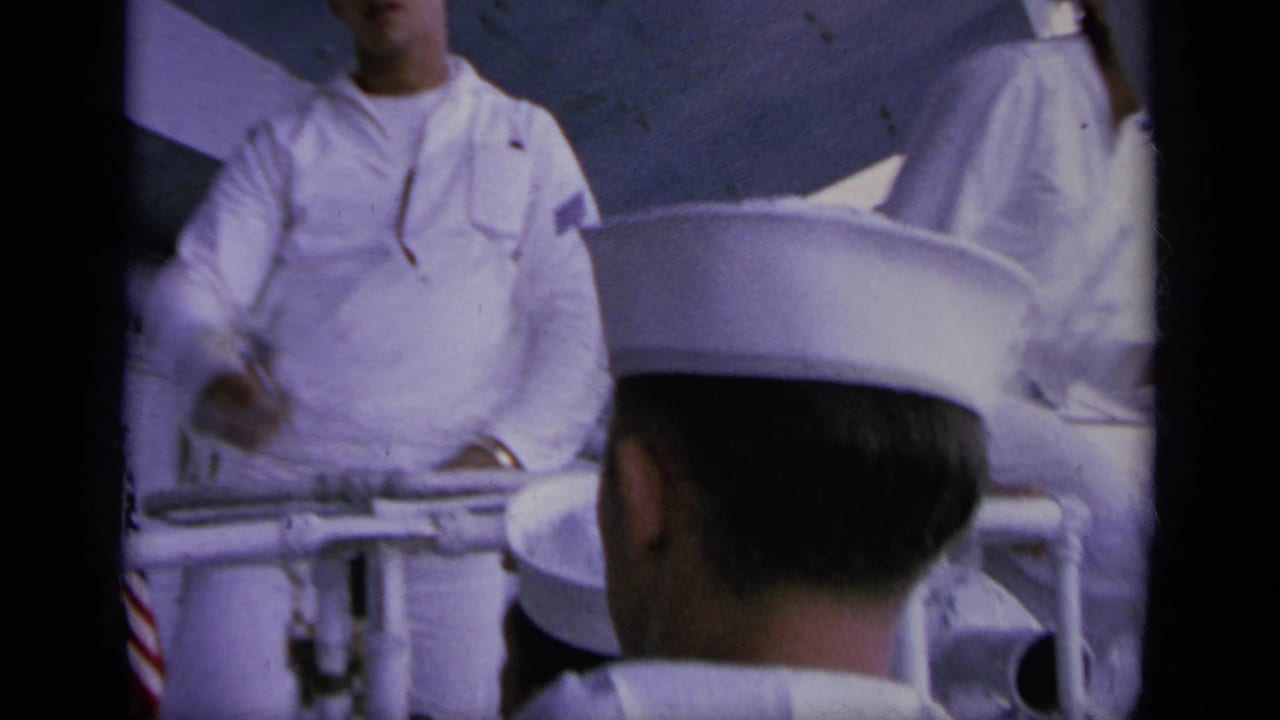 Sailors in white uniforms stand near ship railings on a carrier deck.