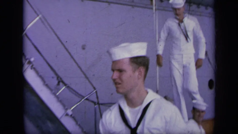 Sailors in white uniforms are seen beside carrier deck stairs and railings, with ship surfaces filling the background.