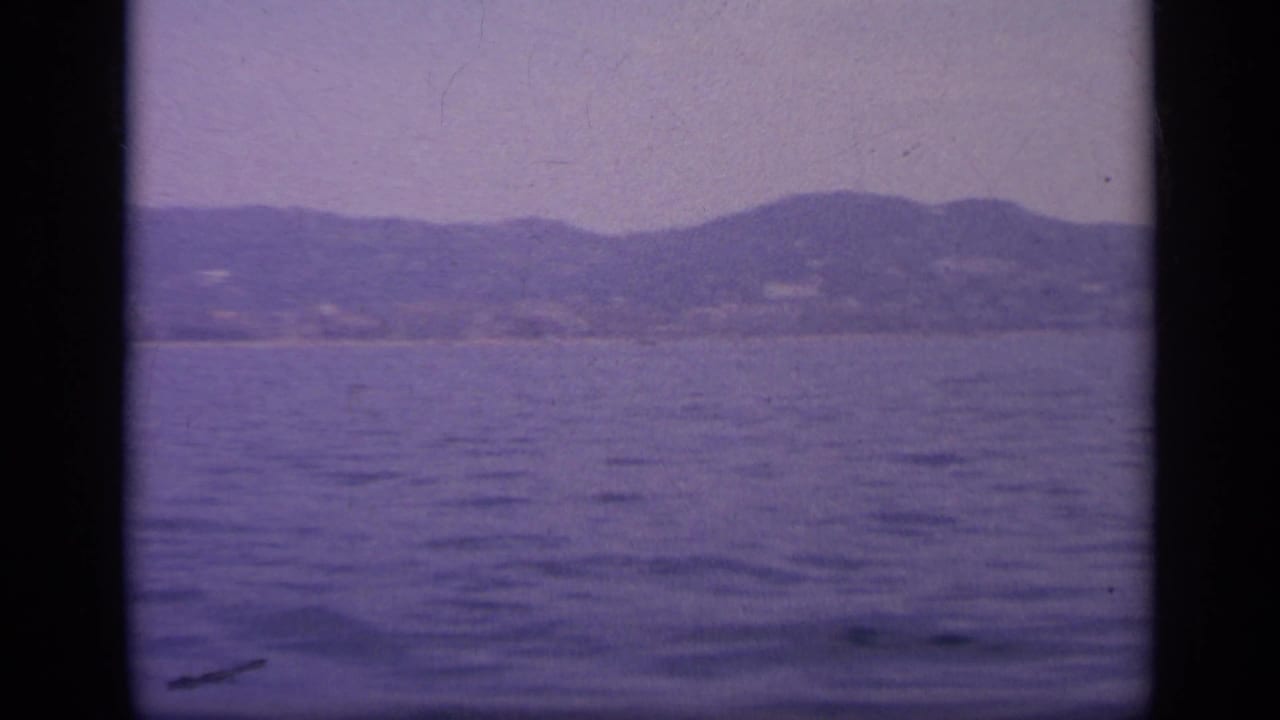 1963 Greece 8mm frame showing open water from the ship, with a subdued coastline and hills softened by haze and film grain.