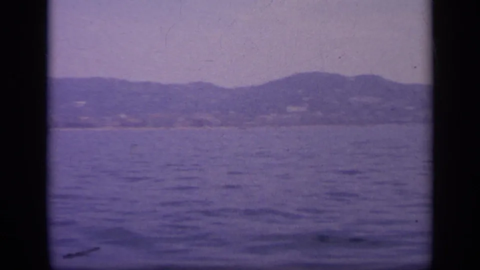 1963 Greece 8mm frame showing open water from the ship, with a subdued coastline and hills softened by haze and film grain.