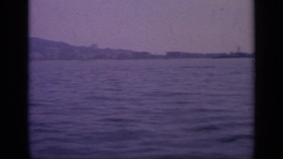 1963 Greece 8mm frame looking over rippled water toward a low, distant shoreline partly obscured by haze and frame borders.