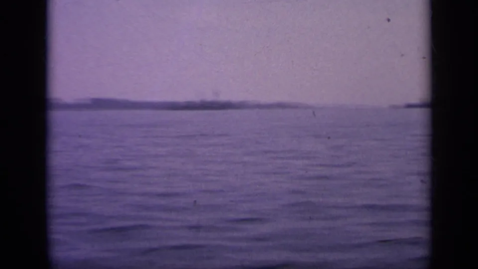 1963 Greece 8mm frame showing calm water, a hazy purple sky, and distant shoreline or landforms on the horizon.