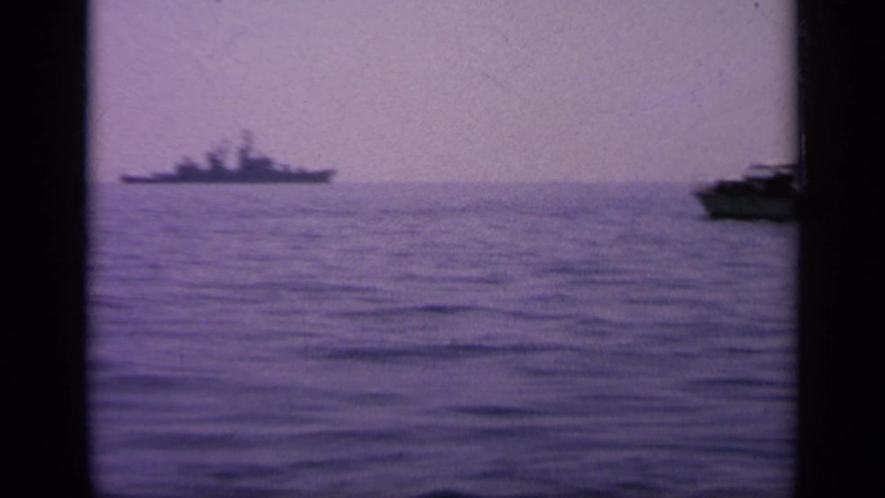 1963 Greece 8mm frame with a distant naval warship silhouette across calm water under a hazy sky.